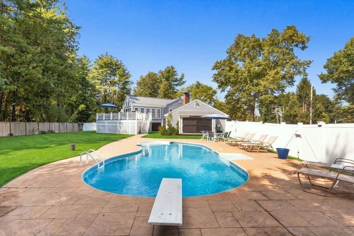 Backyard swimming pool with diving board, patio seating, lawn, and raised deck.