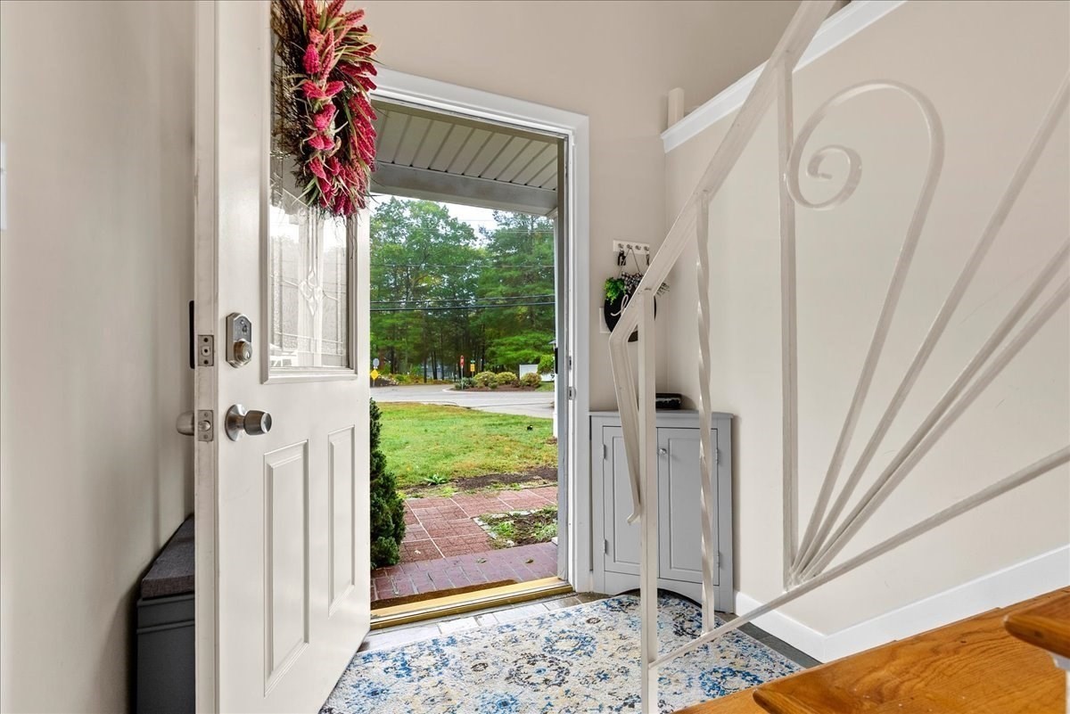 Home entryway with an open front door, patterned rug, and white staircase with decorative railing.