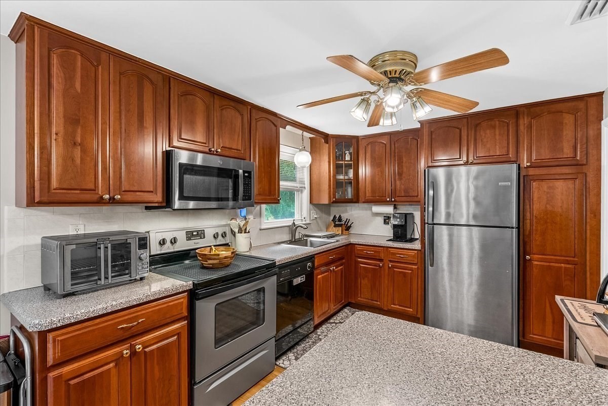 Kitchen with reddish-brown wood cabinets, speckled countertops, and stainless steel appliances.
