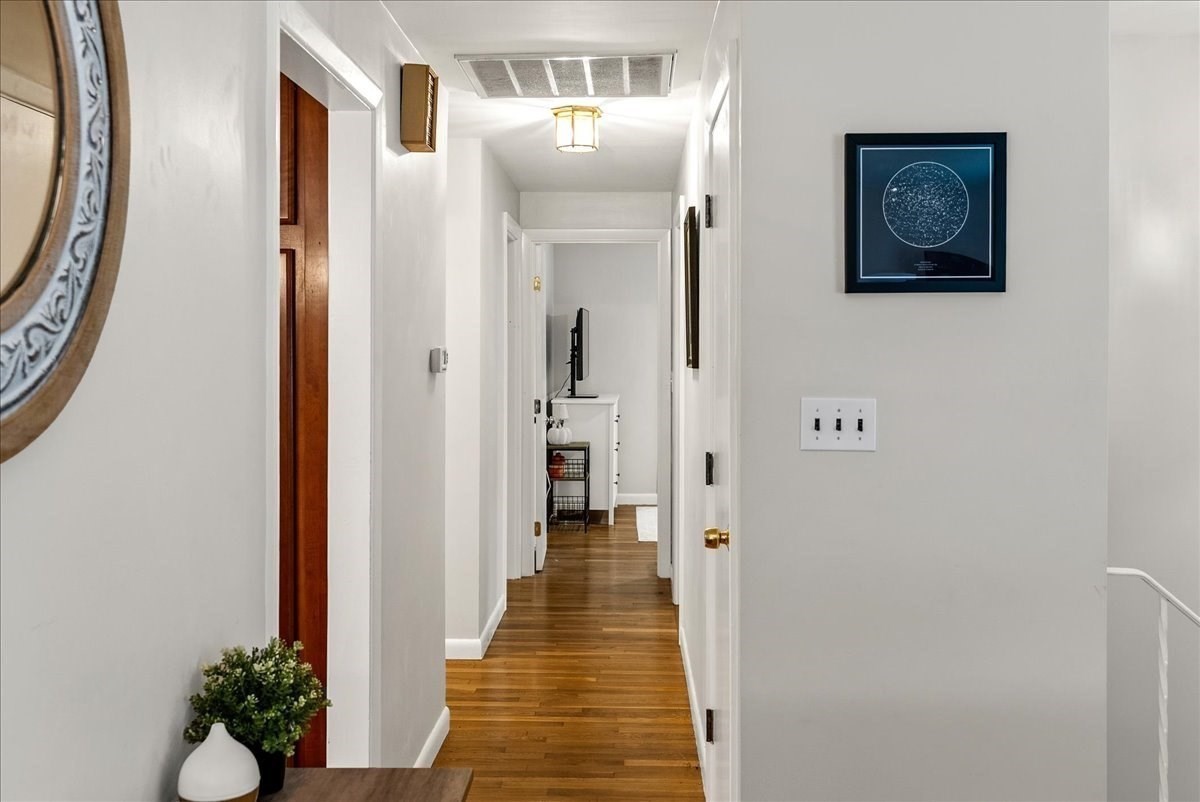 Hallway with hardwood floors, white walls, framed artwork, and a small console at the far end.