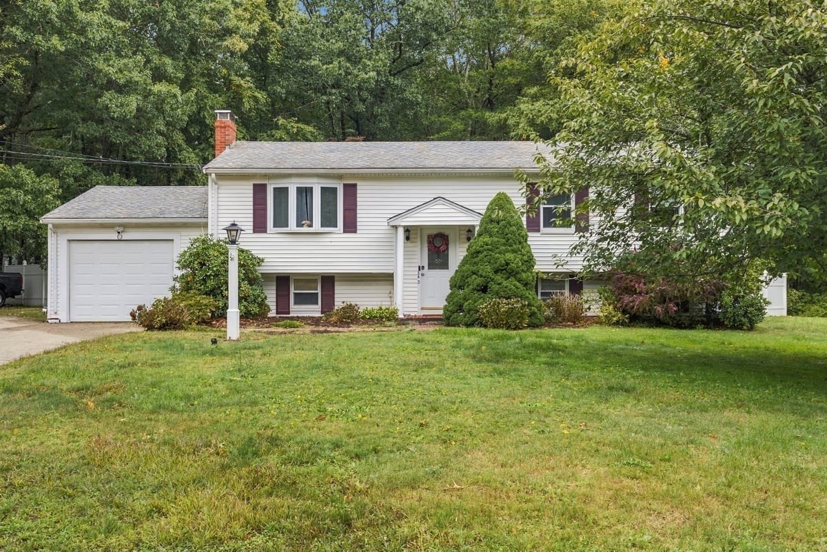 White split-level home with burgundy shutters, attached garage, and a tree-lined lawn.