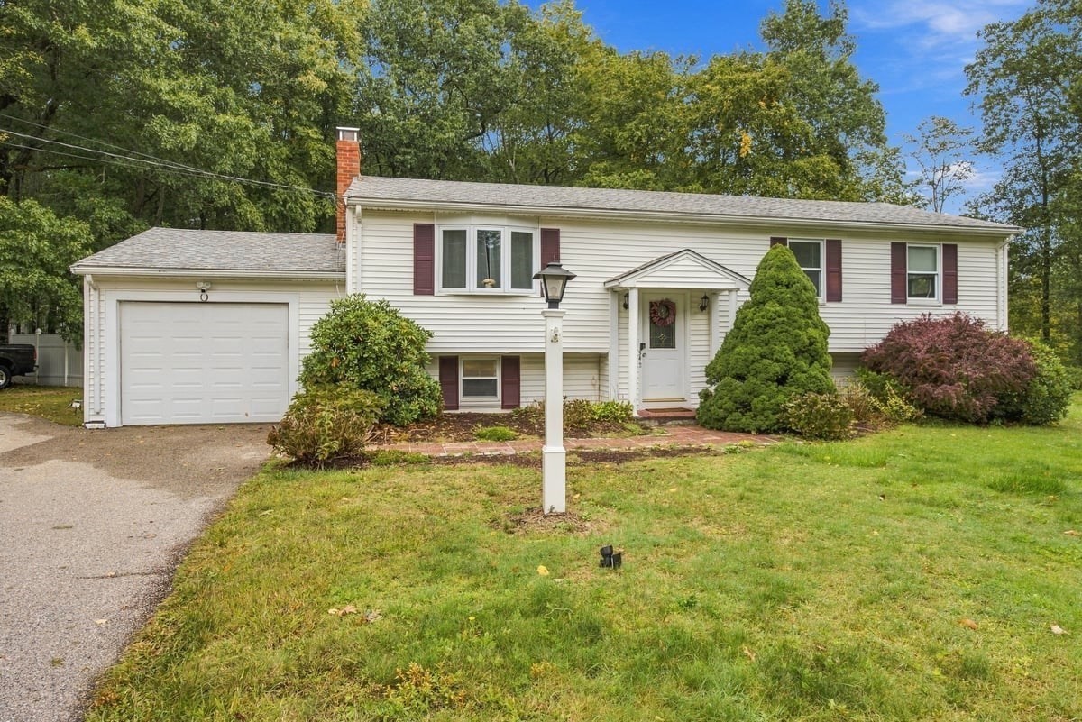 White split-level home with burgundy shutters, attached garage, and leafy front yard.