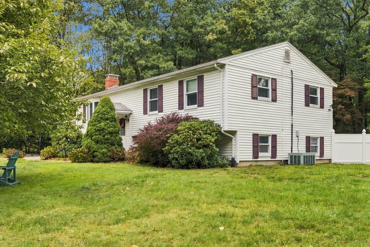 White split-level home with burgundy shutters, a brick chimney, and mature trees.