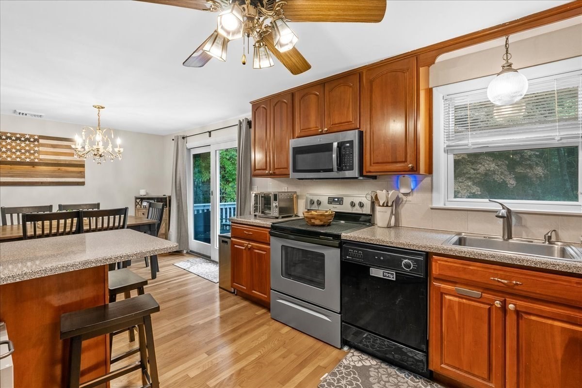 Kitchen with wood cabinetry, stainless steel appliances, and a granite island with bar stools.