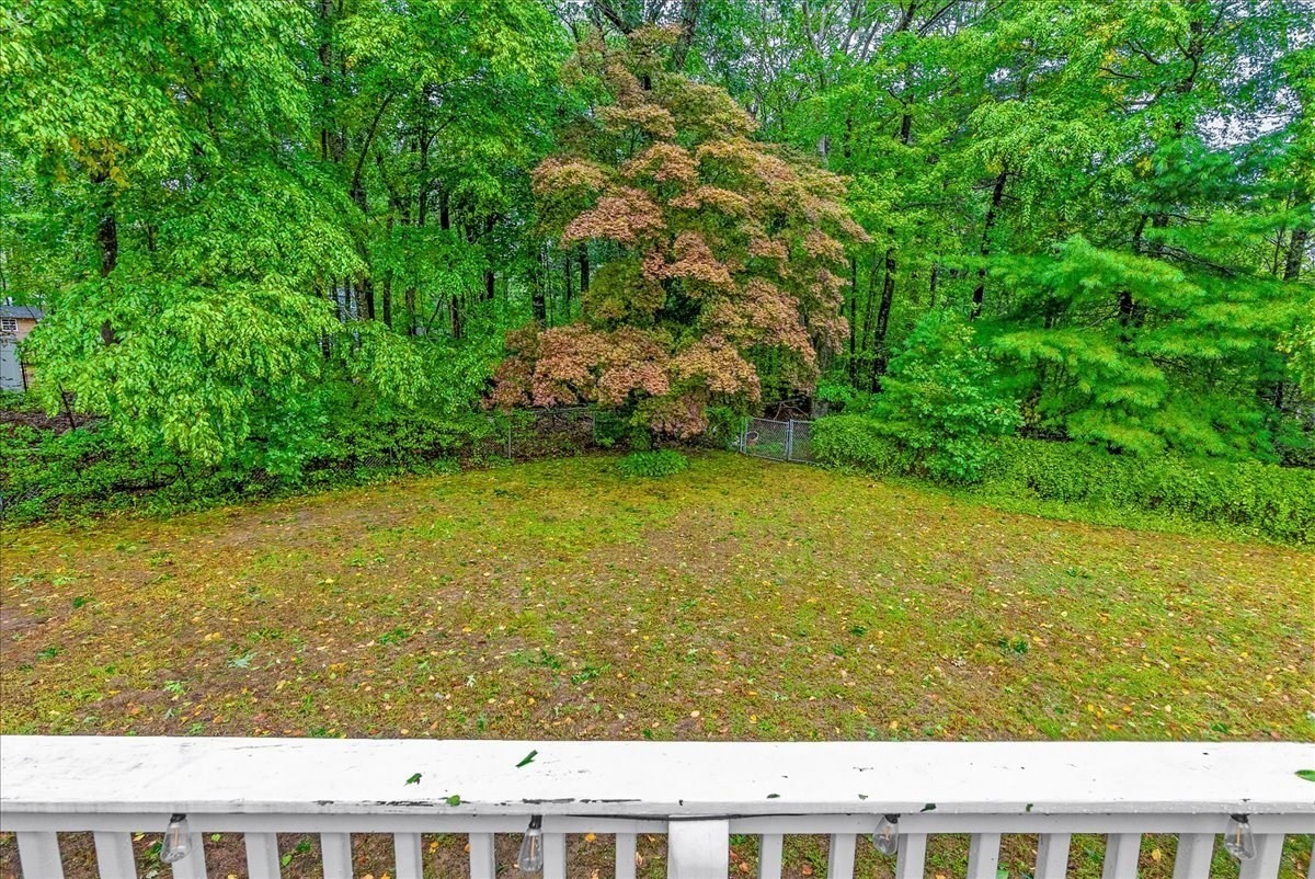 Grassy backyard bordered by mature trees and woodland, viewed over a white deck railing.