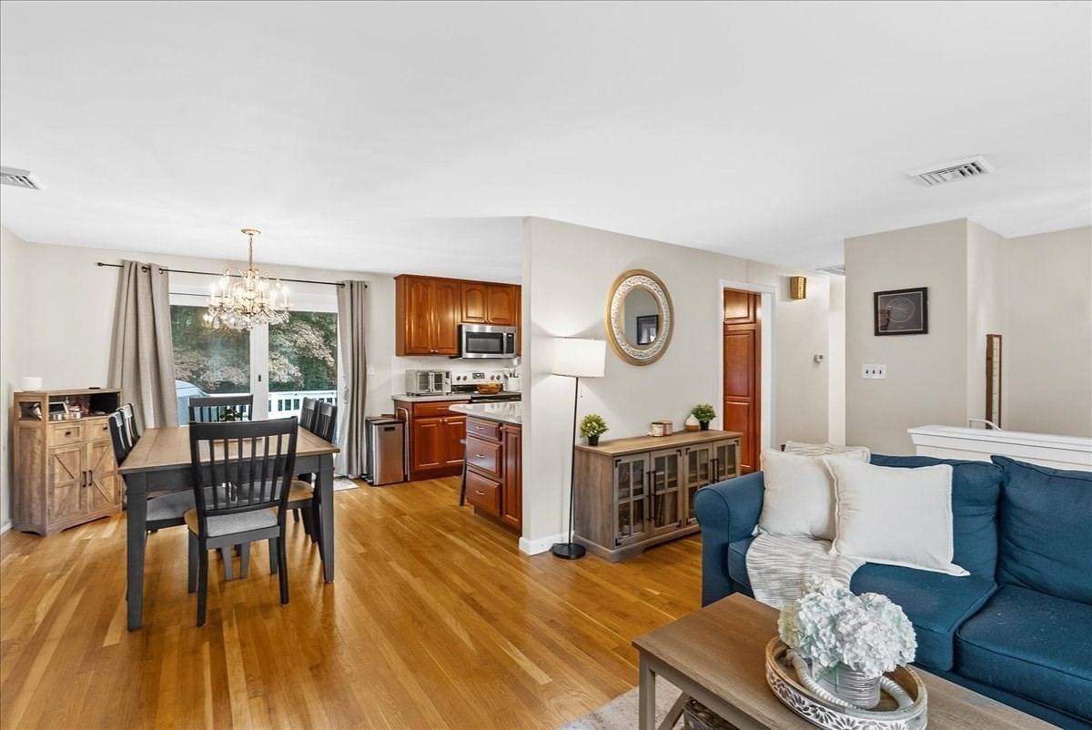 Open-plan living and dining area with a blue sofa, hardwood floors, and wood kitchen cabinetry.