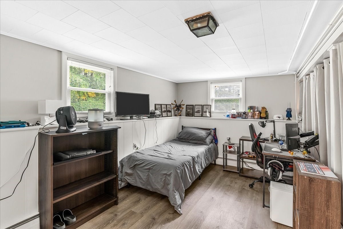Bedroom with a single bed, desk and office chair, dark wood shelving, and two windows.