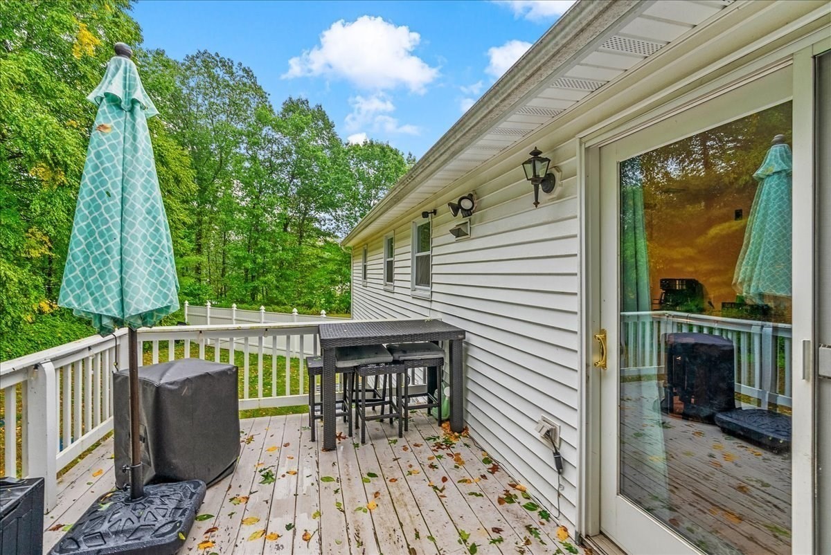 Wooden deck with bar-height table, closed turquoise umbrella, and leafy trees beyond the railing.
