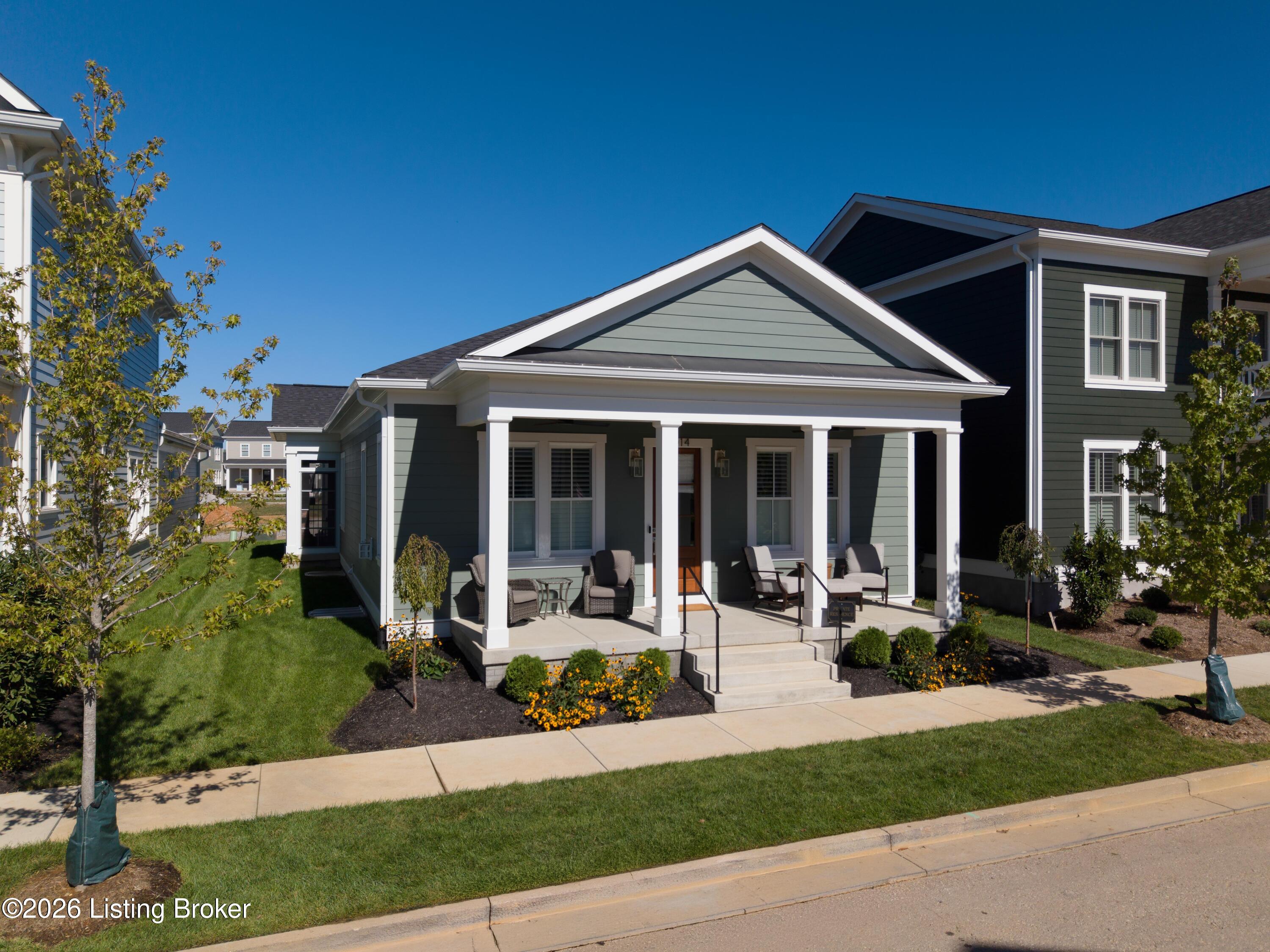 Gray-green house with a white-columned front porch, outdoor seating, and flower beds.