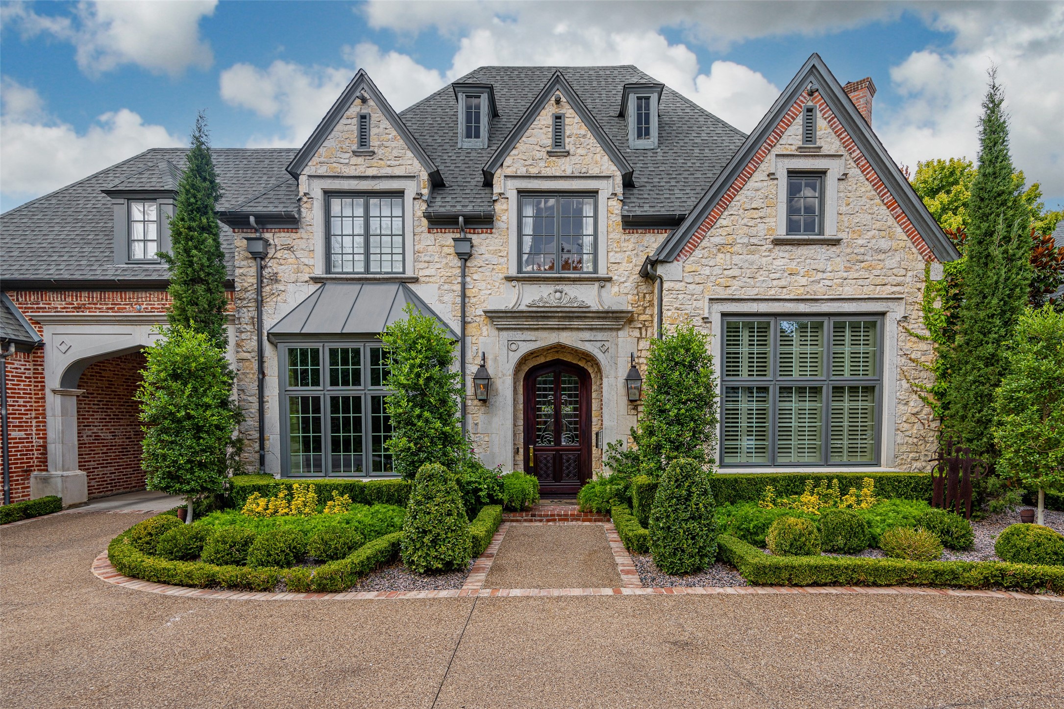 Stone and brick house with steep gables, an arched entry, and manicured landscaping.