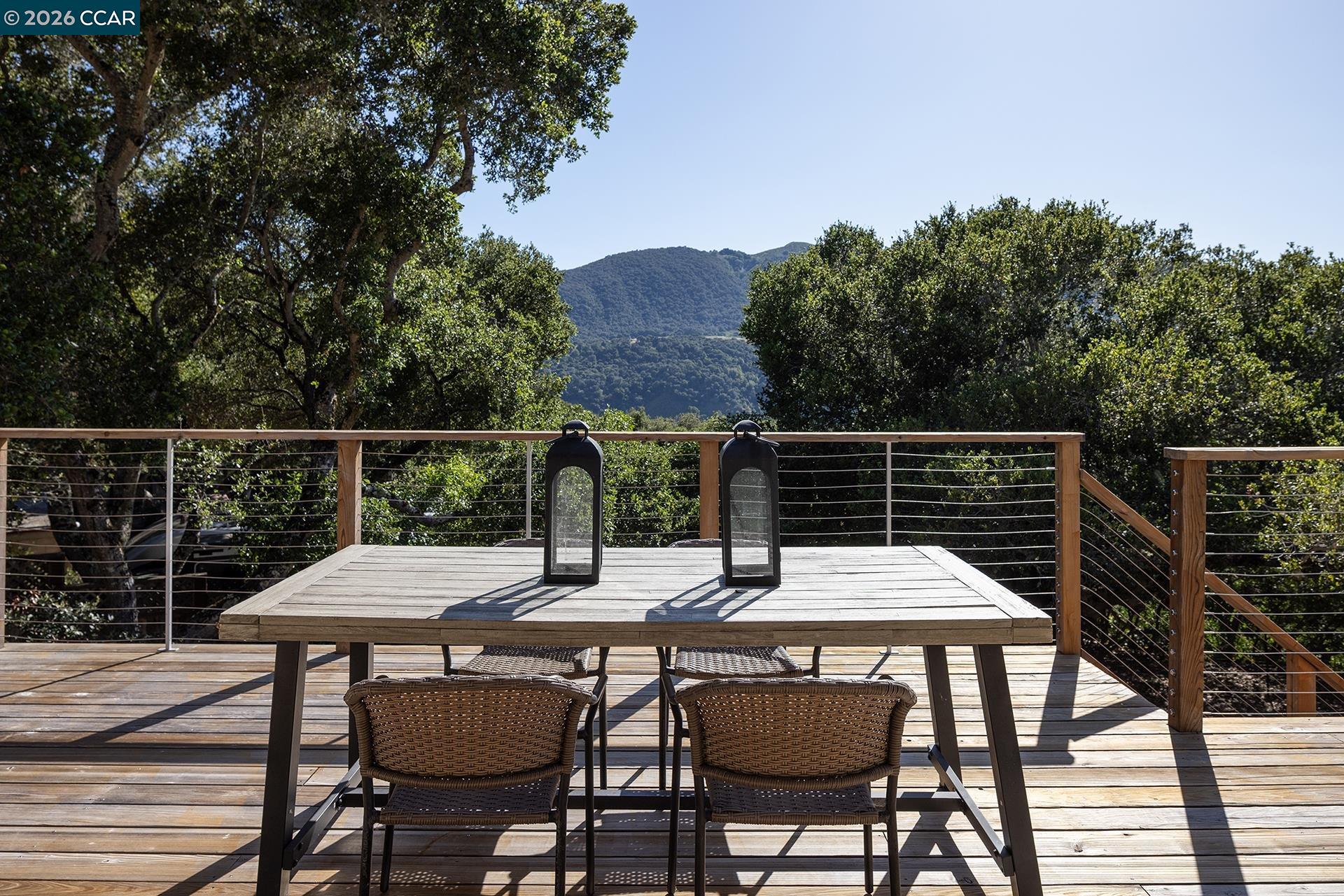 Wood deck dining area with cable railing overlooks wooded hills and a mountain ridge.