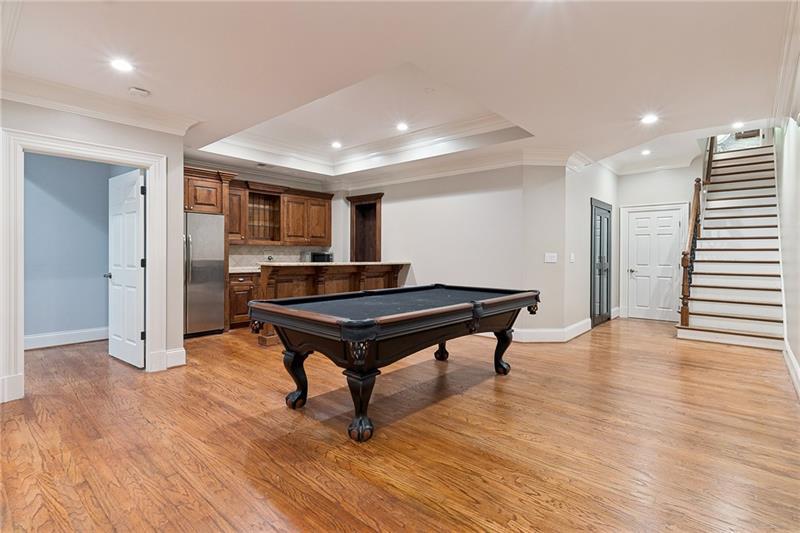 Recreation room with a black pool table, hardwood floors, and a wood-cabinet wet bar.