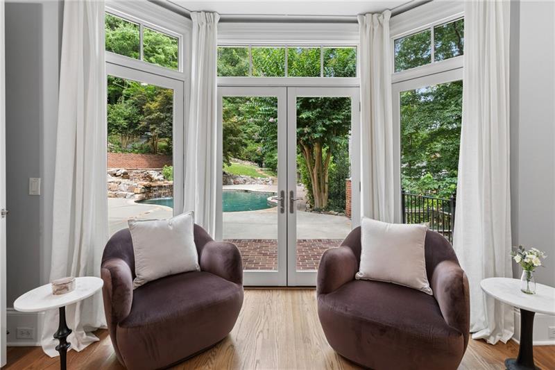 Sitting area with two armchairs facing glass doors overlooking a backyard pool and trees.