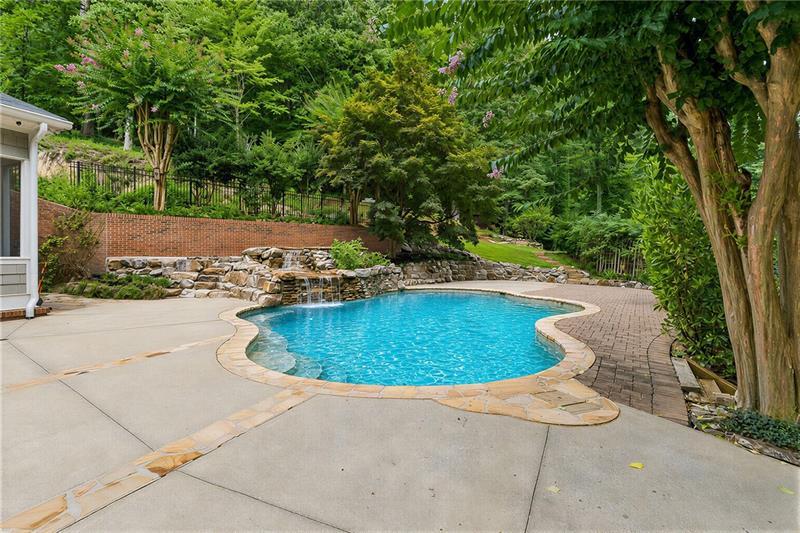 Curving backyard swimming pool with a small rock waterfall and stone-edged patio.