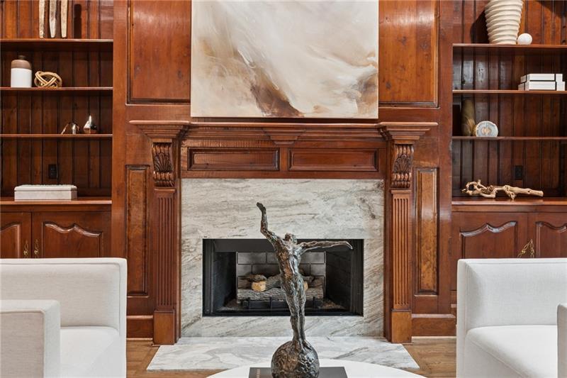 Living room with a marble fireplace framed by carved wood cabinetry and built-in shelves.