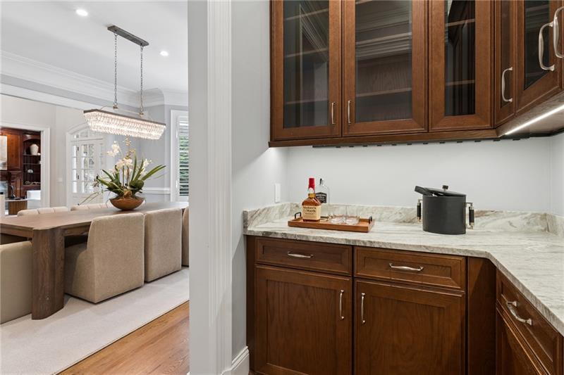 Kitchen beverage nook with dark wood cabinets and stone counter beside a chandelier-lit dining area.