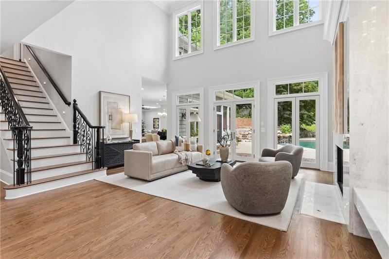 Two-story living room with a curved staircase, tall windows, hardwood floors, and views of a swimming pool.