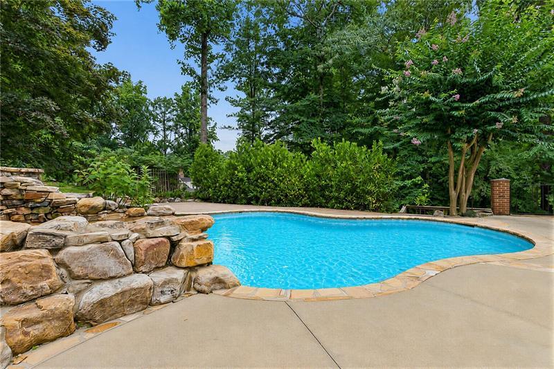 Curved backyard pool beside a stacked-stone wall and mature landscaping.