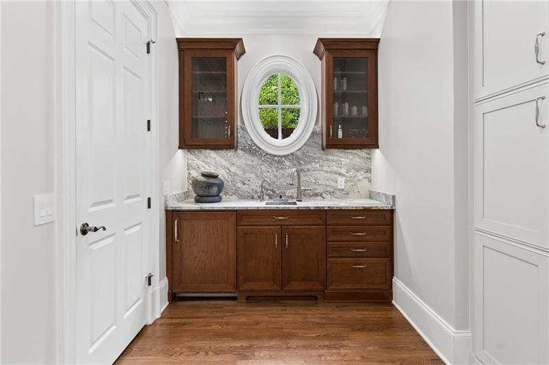 Butler’s pantry with dark wood cabinets, marble surfaces, and an oval window.