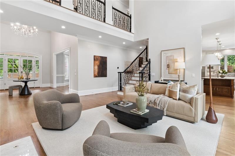 Double-height living room with pale seating, hardwood floors, and a wrought-iron staircase.