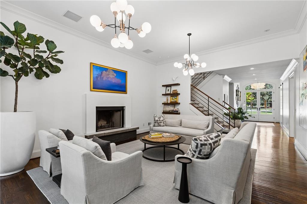 Staged living room with white sofas, a fireplace, tall ceilings, and a staircase.