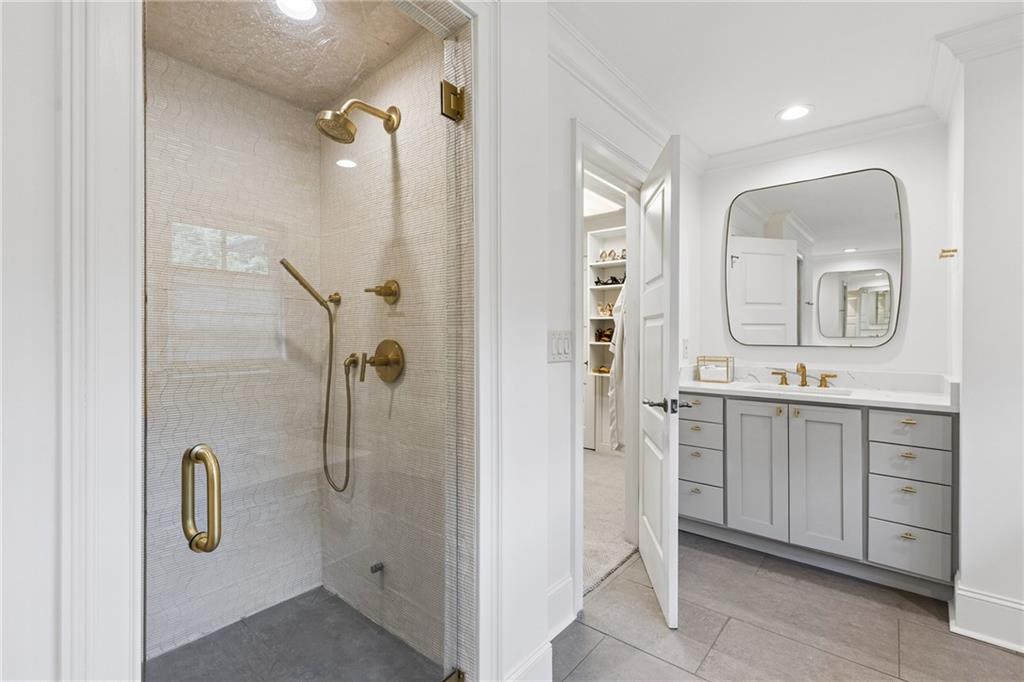 Bathroom with a brass-fixture glass shower beside a white vanity and rounded mirror.