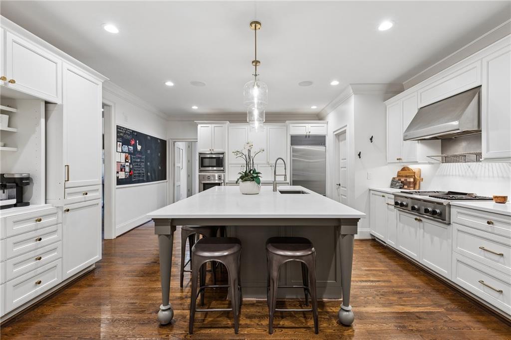 White kitchen with a large island, stainless steel appliances, and warm hardwood floors.