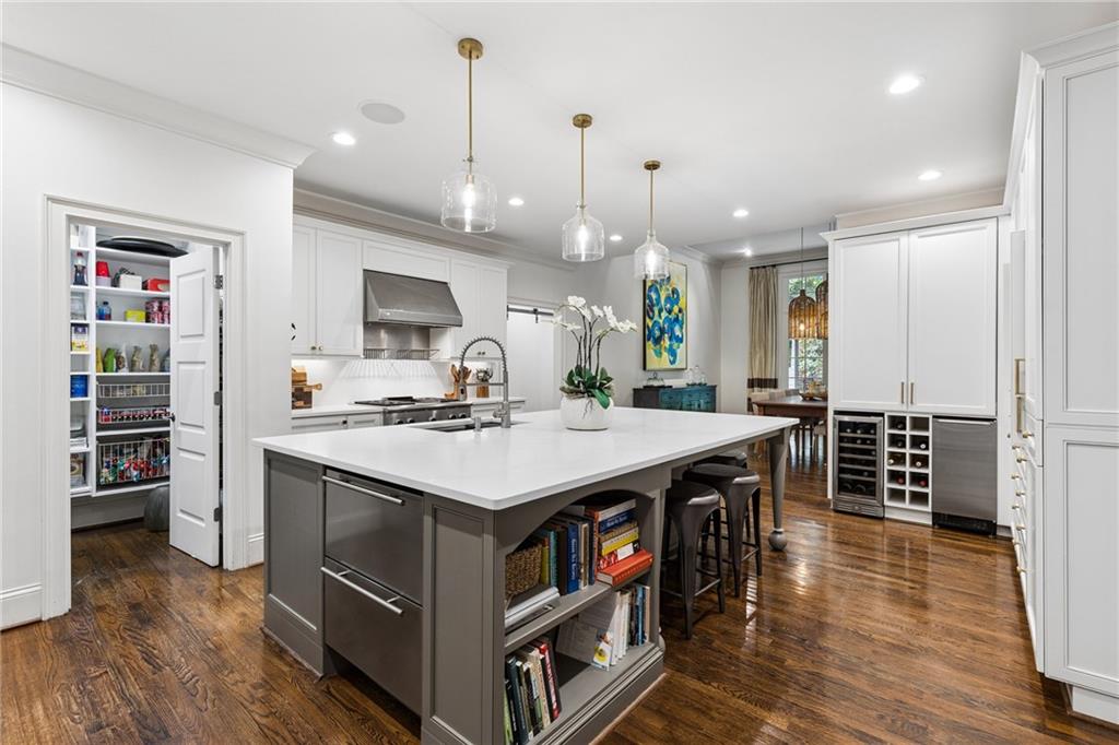 Kitchen with a large gray island, pendant lights, hardwood floors, and an open walk-in pantry.