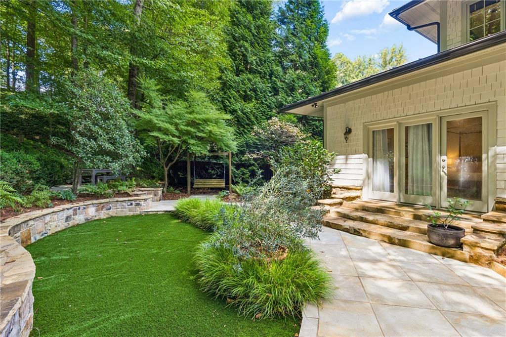 Backyard patio with stone terrace, small lawn, garden swing, and mature trees.