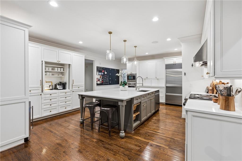 Kitchen with a large gray island, white cabinetry, stainless-steel appliances, and hardwood floors.