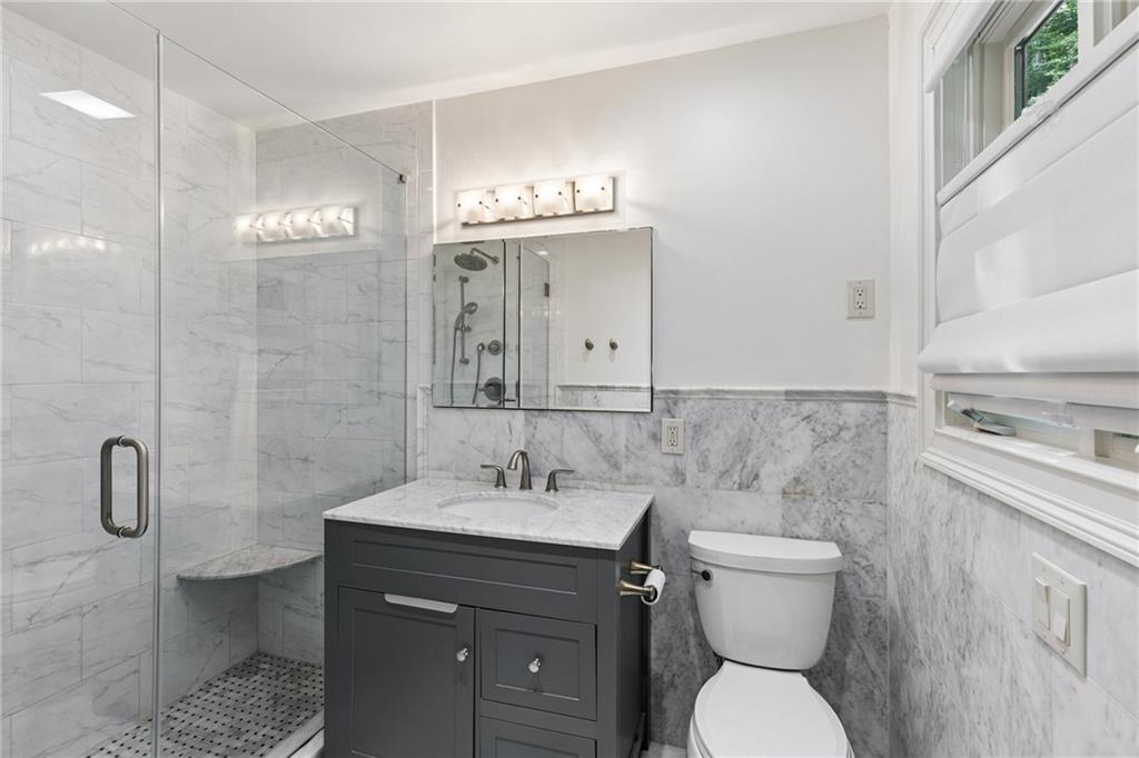 Bathroom with marble-look tile, glass shower and built-in bench, dark vanity, and window.