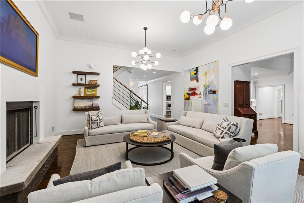 Staged living room with light seating around a round coffee table, fireplace, and staircase.