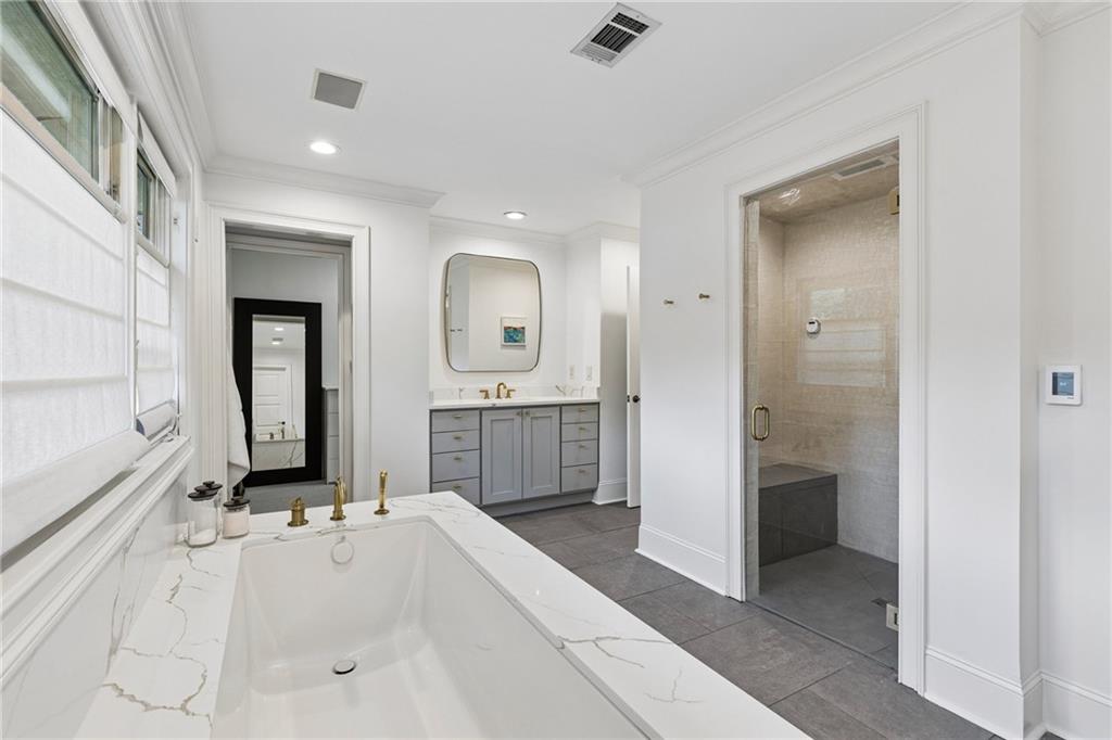Bathroom with a large soaking tub, gray double vanity, and glass-enclosed tiled shower.