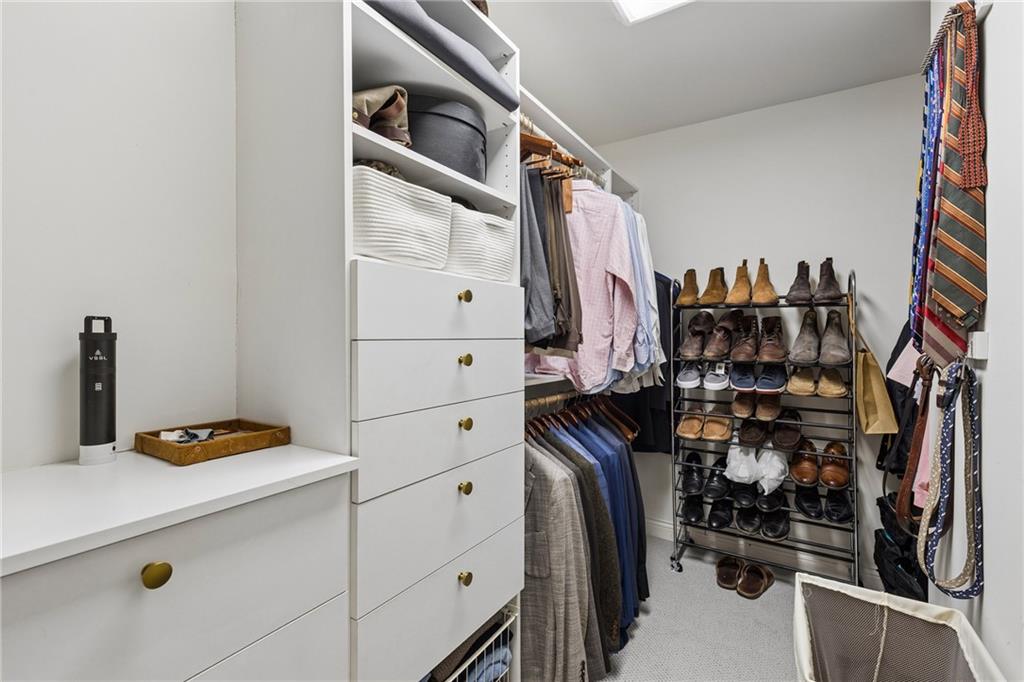 Walk-in closet with white built-in storage, hanging clothes, and a freestanding shoe rack.