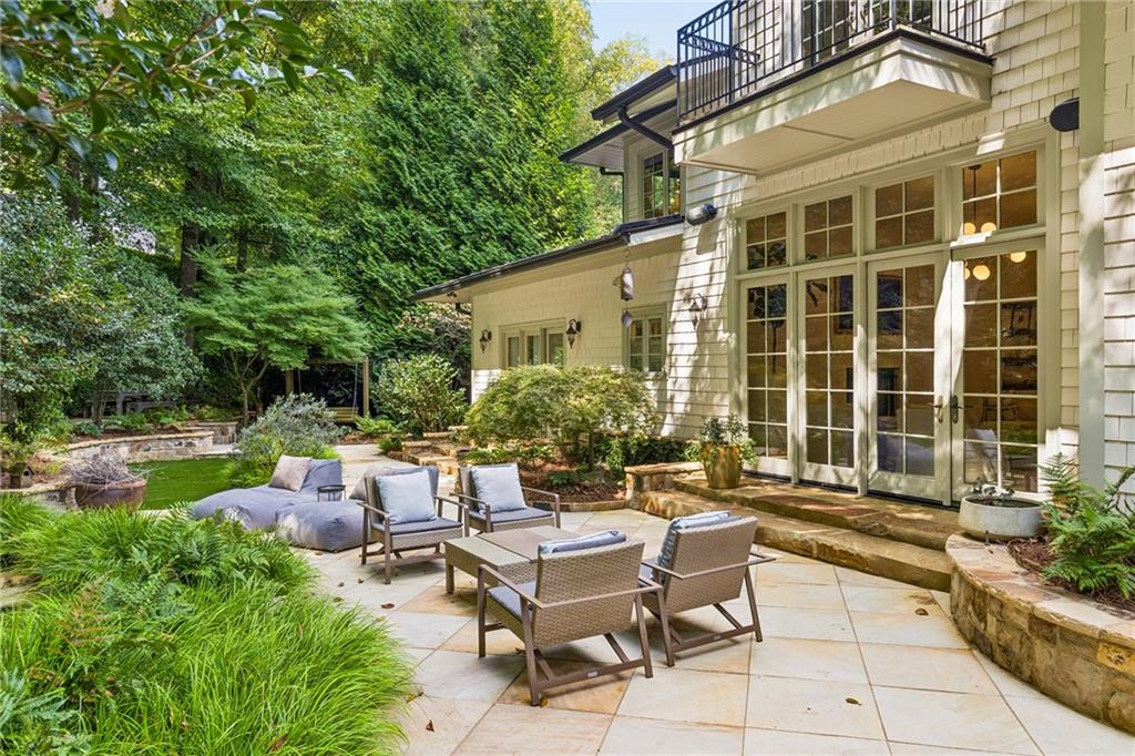 House’s rear patio with French doors, outdoor seating, and lush garden plantings.