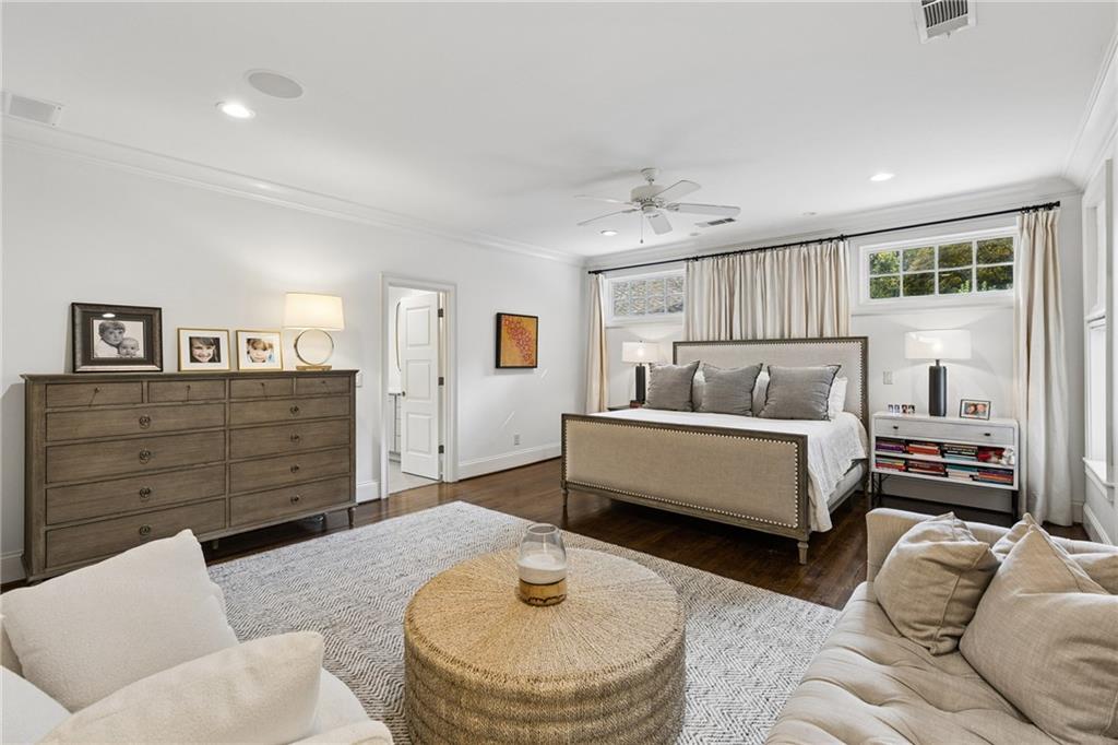 Furnished bedroom with a centered bed, curtained windows, wooden dresser, and seating area.
