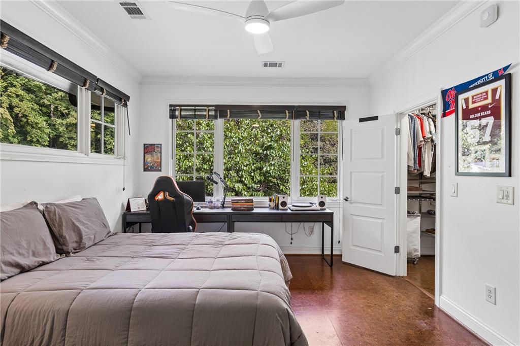 Bedroom with a desk beneath wide windows overlooking leafy trees, a bed, and polished wood flooring.
