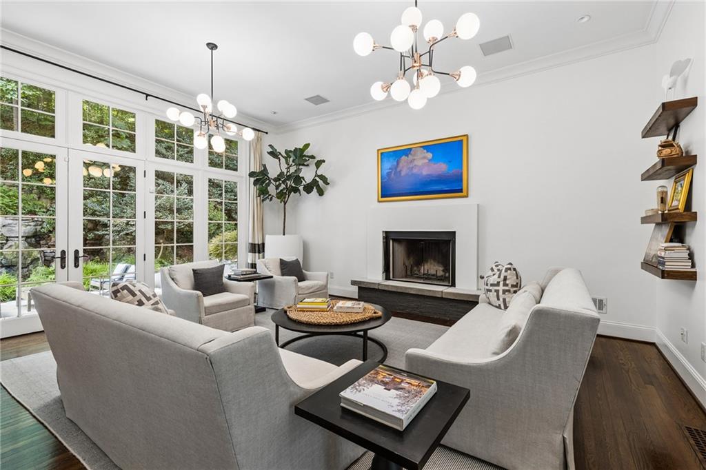 Living room with a fireplace, gray seating, and tall French doors overlooking greenery.