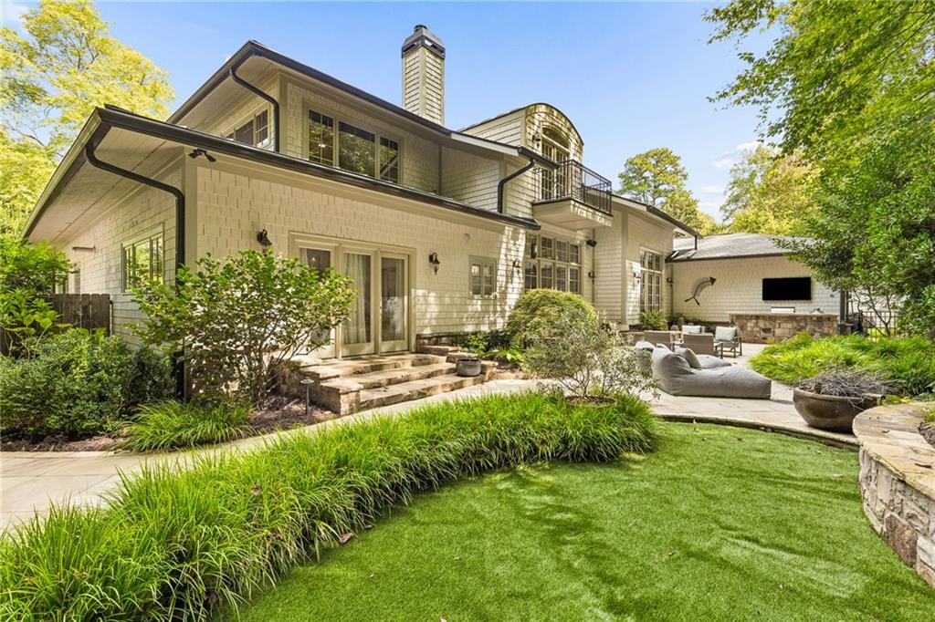 Rear of a two-story house with a balcony, stone patio steps, outdoor seating, and a manicured lawn.