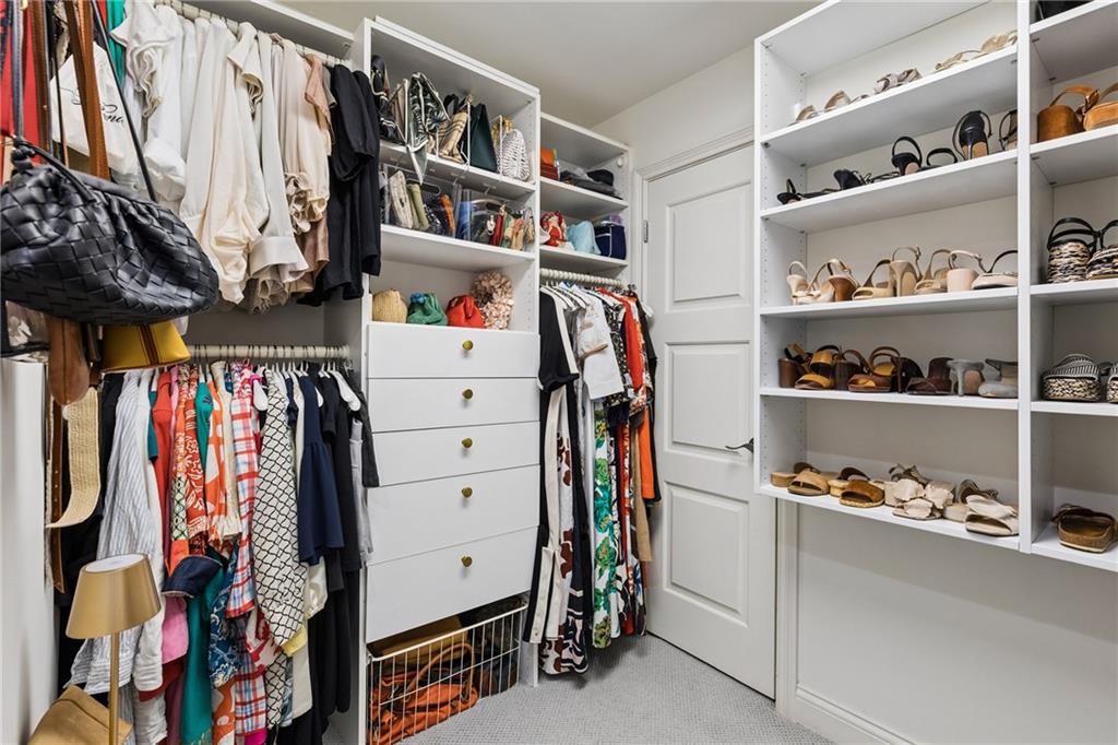 Walk-in closet with built-in white shelving, drawers, hanging clothes, and rows of shoes.