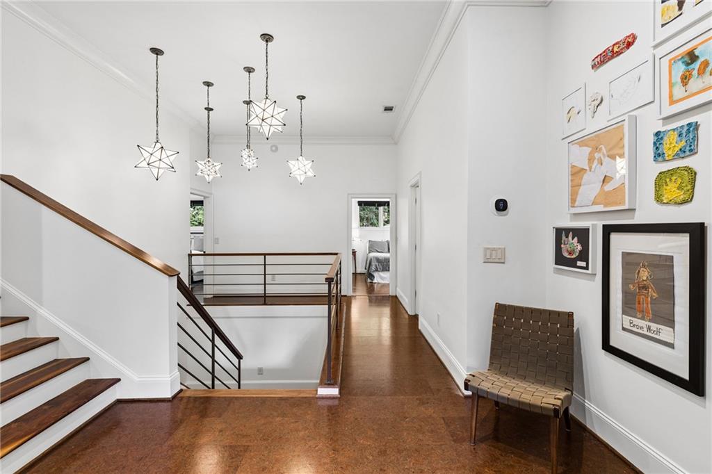 Upstairs foyer with a wooden staircase, geometric pendant lights, and framed artwork along the hallway.
