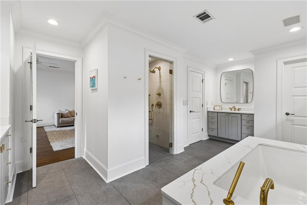 Bathroom with a walk-in shower, gray tile, and a marble-look vanity with gold fixtures.