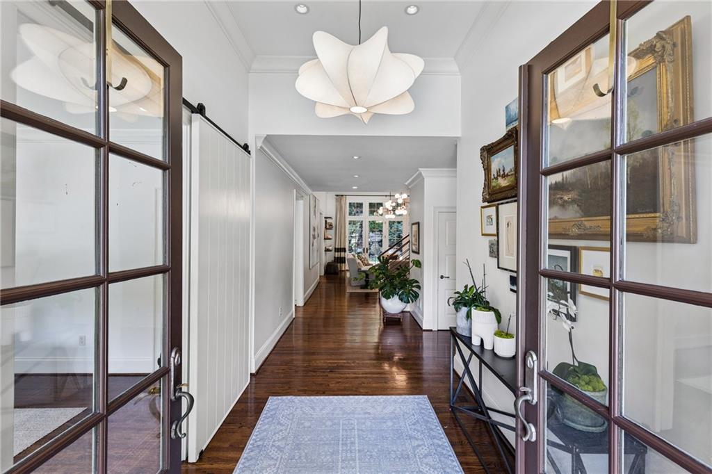 Furnished entry hall with polished hardwood floors, glass-paneled doors, framed art, and potted plants.