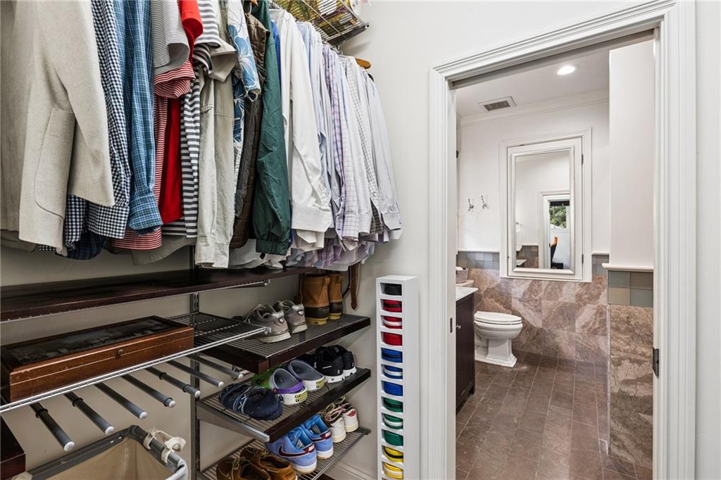 Walk-in closet with organized clothes and shoes opening into a marble-tiled bathroom.