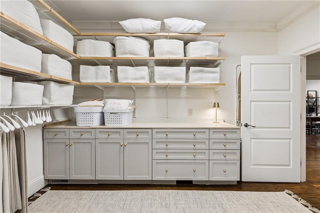 Walk-in closet with folded linens on open shelves, gray built-in cabinets, and hanging clothes.