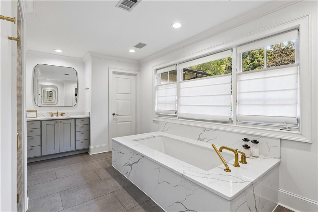 Bathroom with a marble-look soaking tub, brass fixtures, and wide shaded windows.