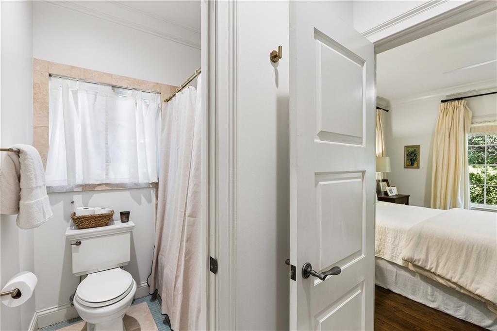 Bathroom with a curtained tub and toilet, viewed through an open door into a bedroom.