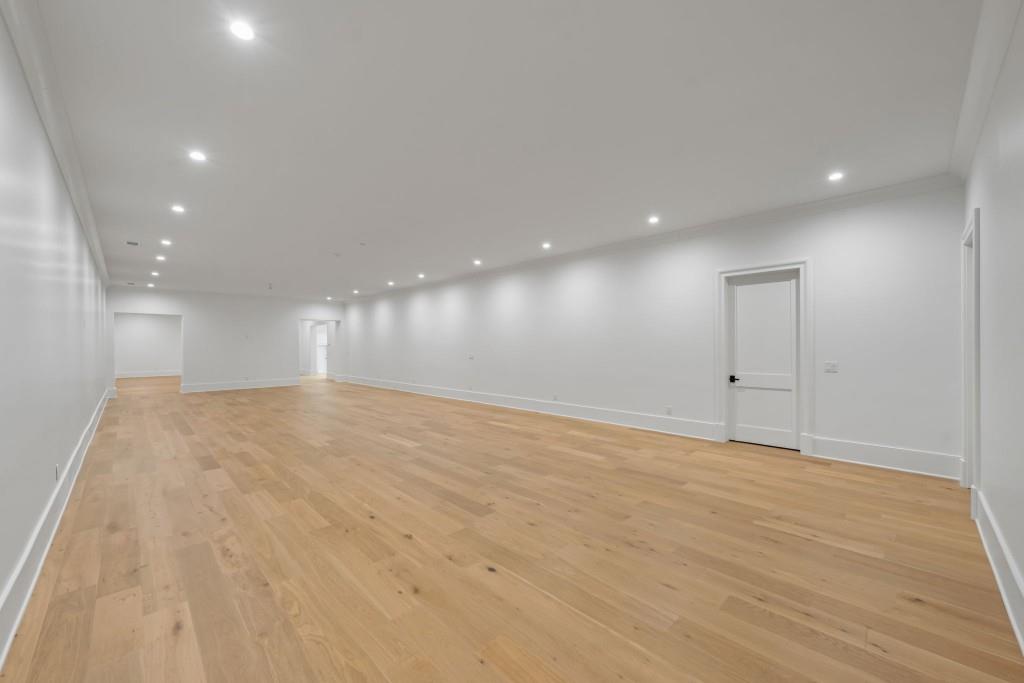Large vacant room with light hardwood flooring, white walls, and recessed lights.