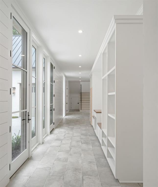 Bright hallway with gray tile floors, white built-in shelving, and glass-paneled exterior doors.