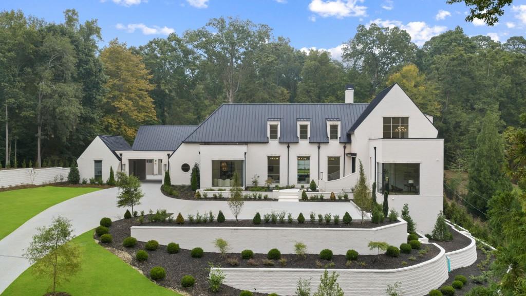 Modern white home with a dark metal roof, curved retaining walls, and landscaped lawn.